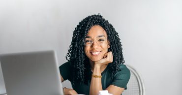 happy ethnic woman sitting at table with laptop